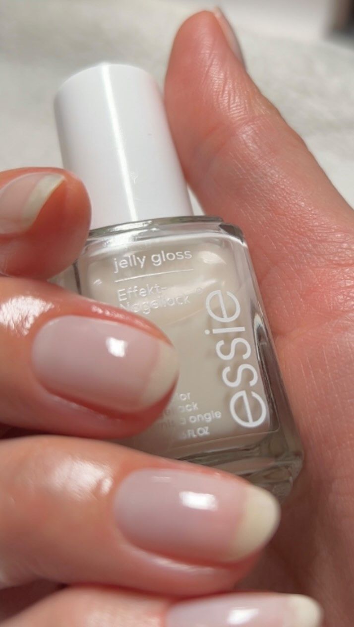 A photo of hands with a milky silk veil nail colour holding a bottle of Essie Jelly Gloss nail polish