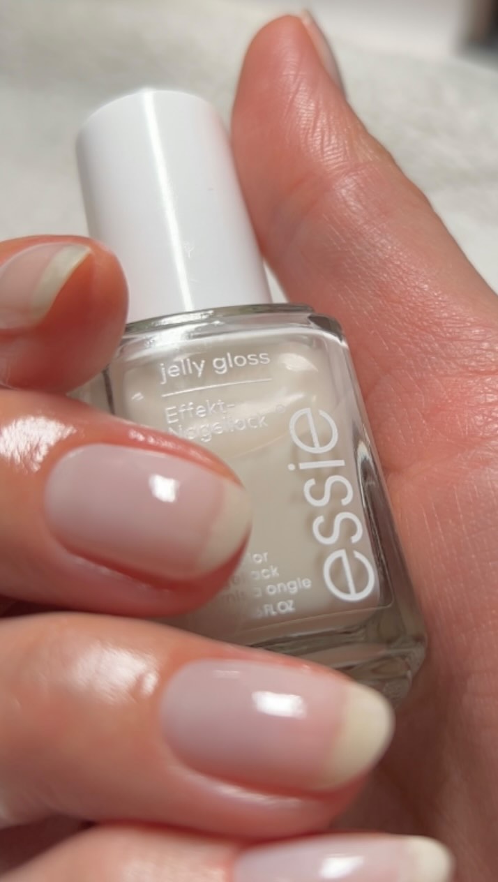 A photo of hands with a milky silk veil nail colour holding a bottle of Essie Jelly Gloss nail polish