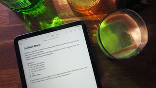iPad (2022) with Notes app open to a cocktail recipe sitting next to a cocktail glass