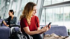 A woman sits at the gate in an airport and looks at her phone.