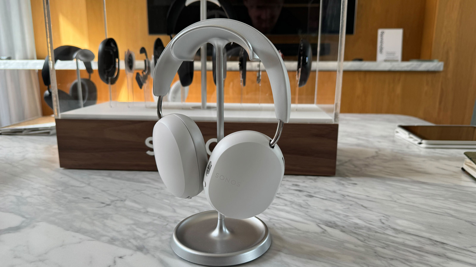 Sonos Ace headphones in soft white hanging on a stand