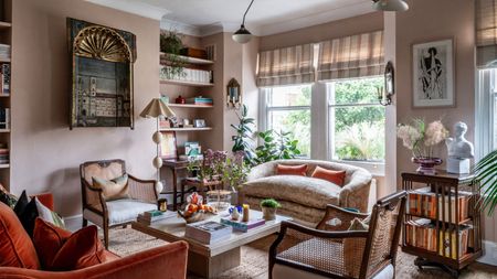 Transitional living room with pale pink walls, orange velvet sofa, midcentury pendant, antique art, marble coffee table with decor