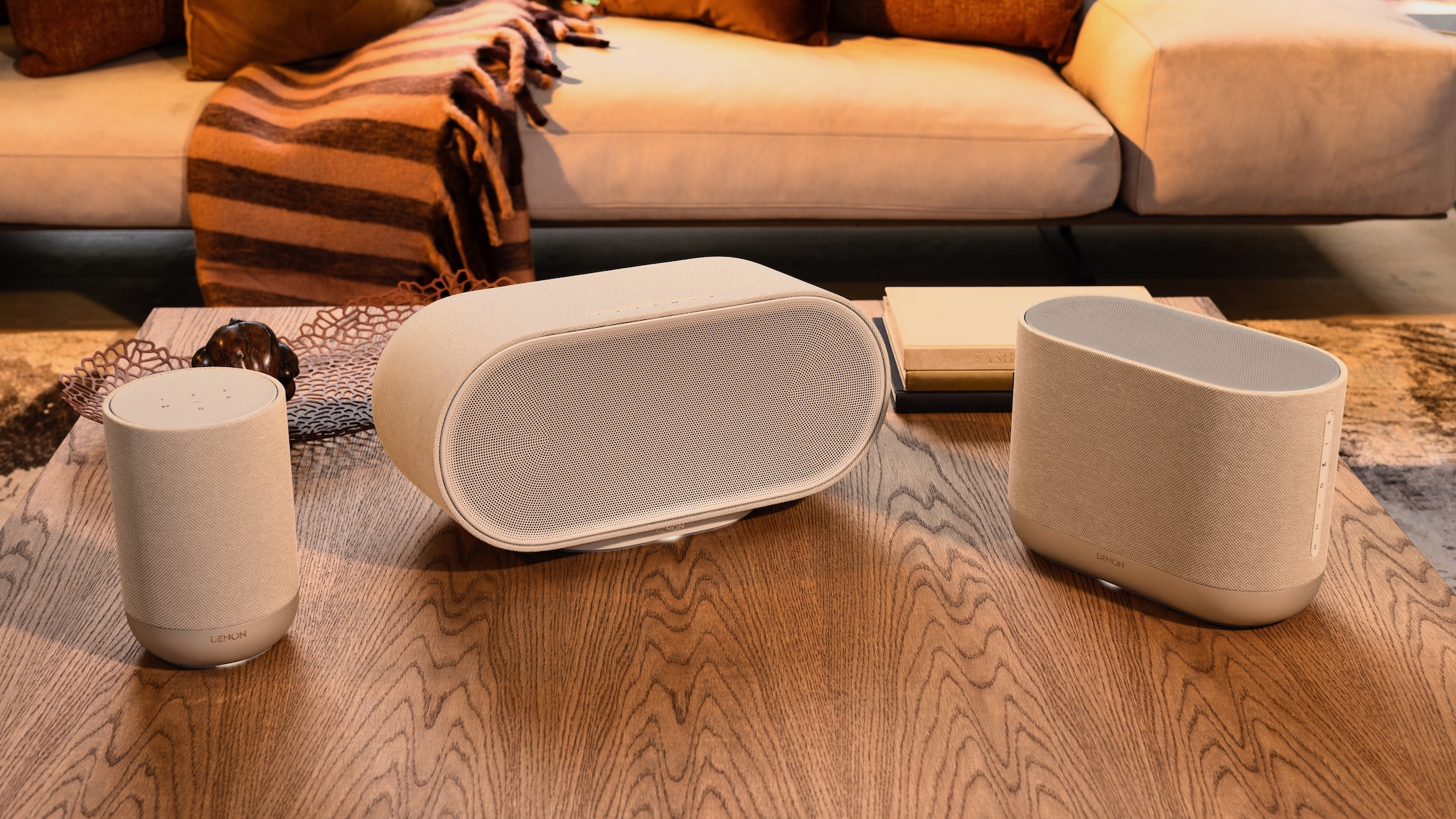 The three new Denon Home speakers in white on a wooden tabletop.