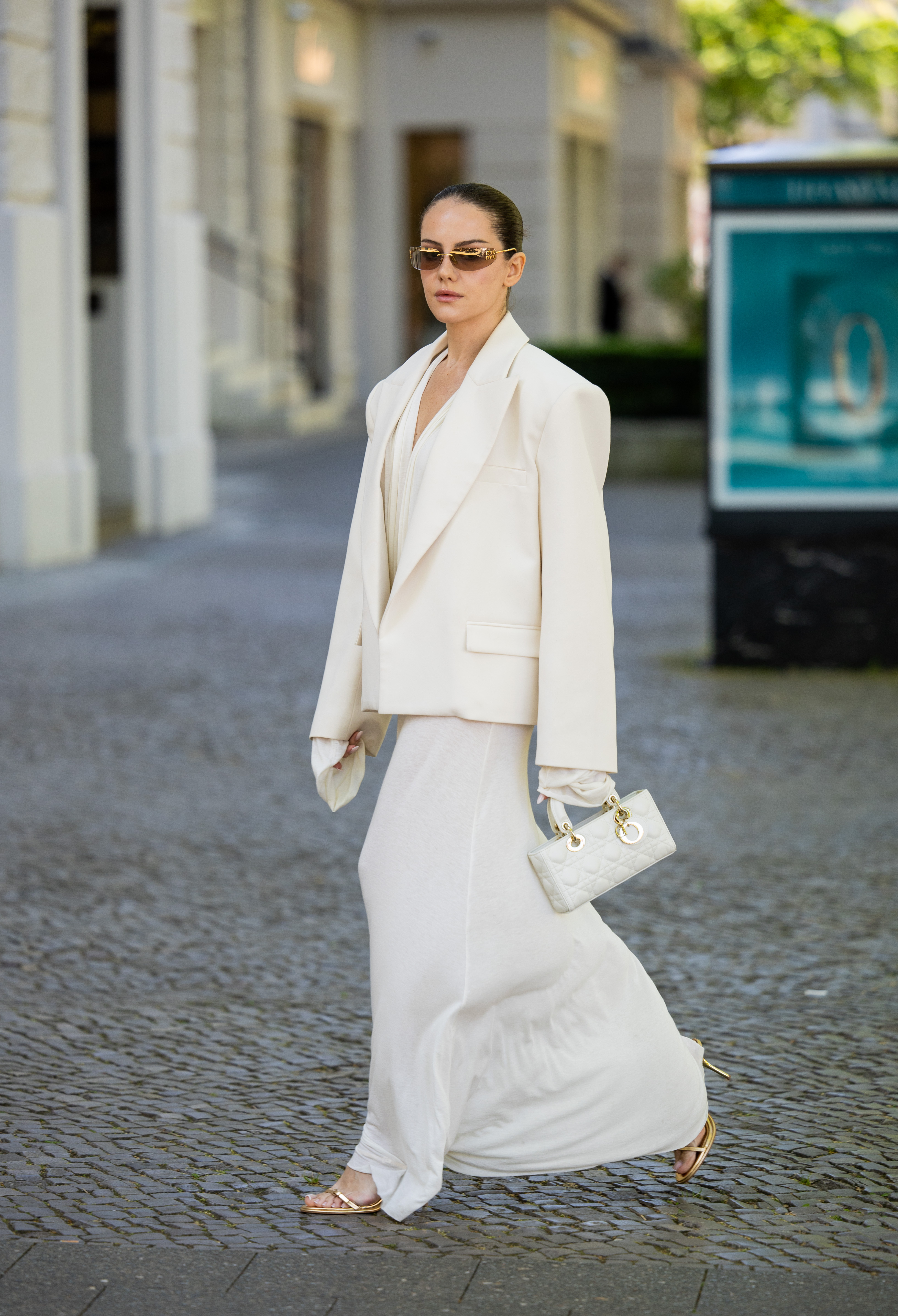 A Couture Fashion Week attendee wears a white blazer and maxi skirt with gold heeled sandals