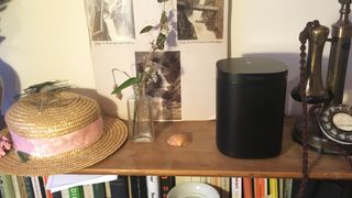A Sonos One in black on a wooden shelf