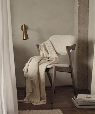 A single upholsered dinging style chair with wooden arms. A blanket draped over it