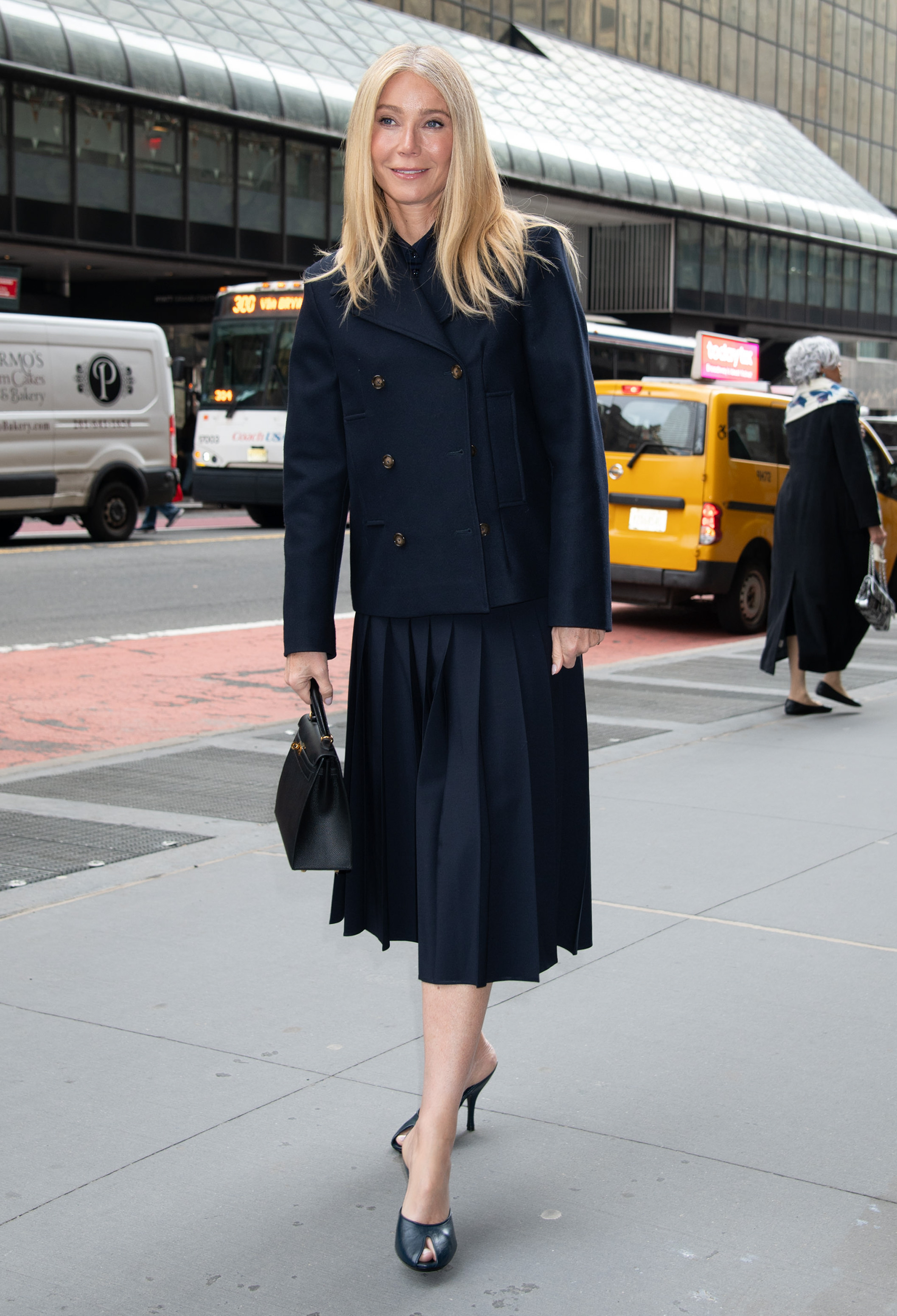 Gwyneth paltrow wears a navy blazer, navy pleated skirt, and navy peep-toe mules.