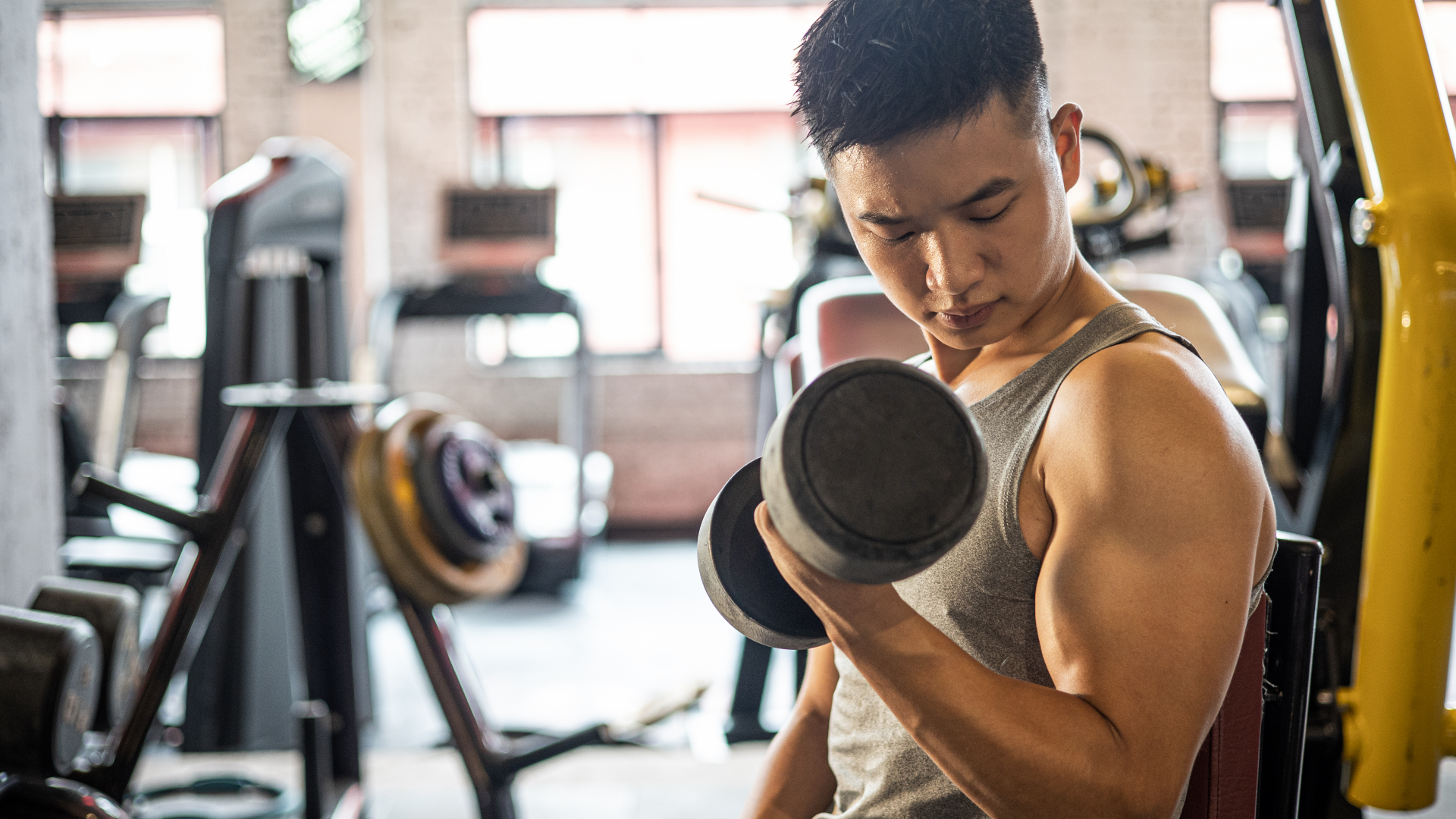 A young man doing bicep curls with dumbbells at the gym