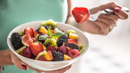 A person holding a bowl of fruits and berries