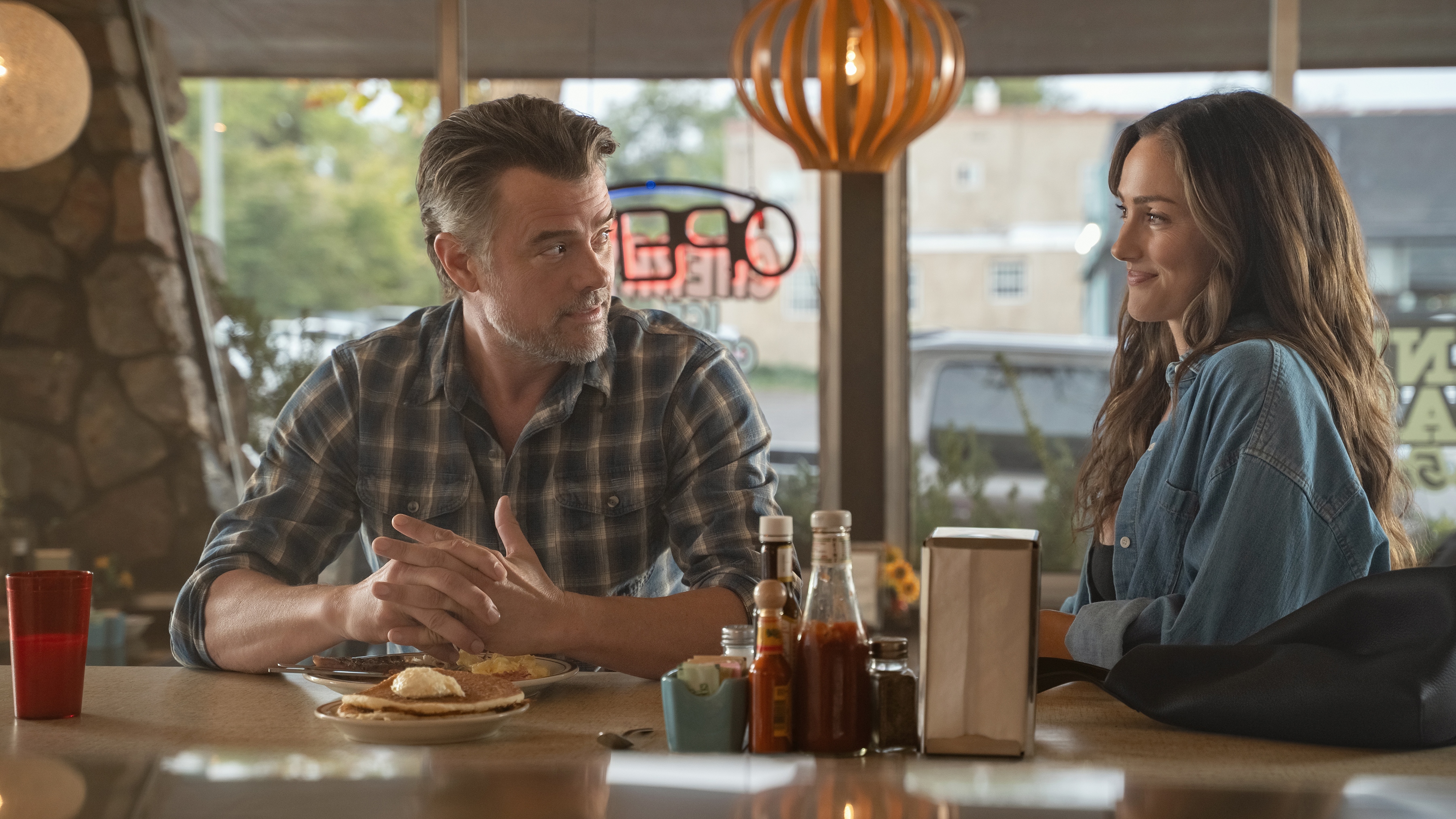 Josh Duhamel as Staten and Minka Kelly as Quinn smiling at each other while sitting at the bar of a diner.