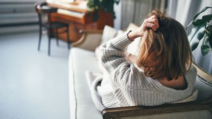 A woman lounging on a couch scrunches her hair in a sign of anxiety