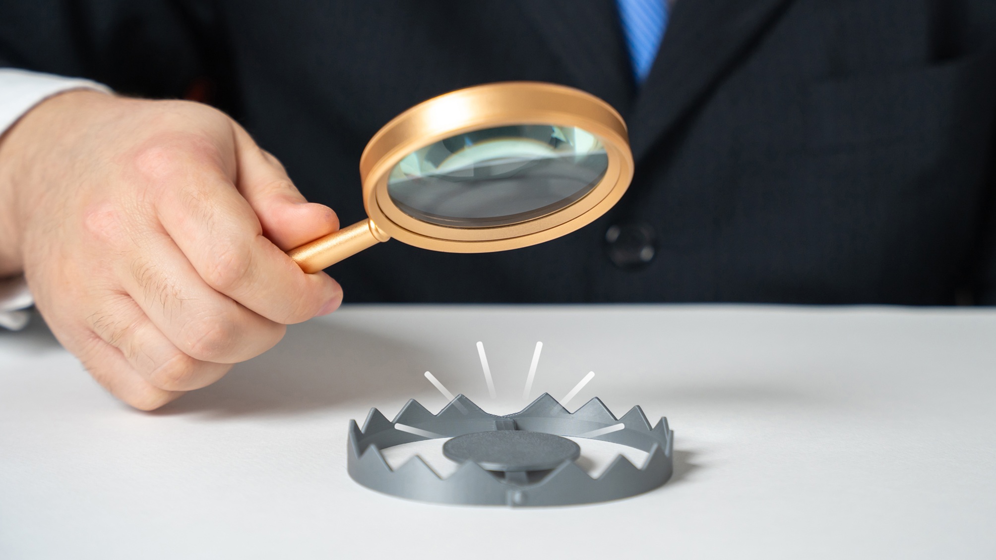 A businessman, only his hand showing, examines a trap with a magnifying glass.