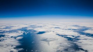 Why is the sky blue? An aerial view of clouds floating over the ocean surrounded by the glow of a blue sky