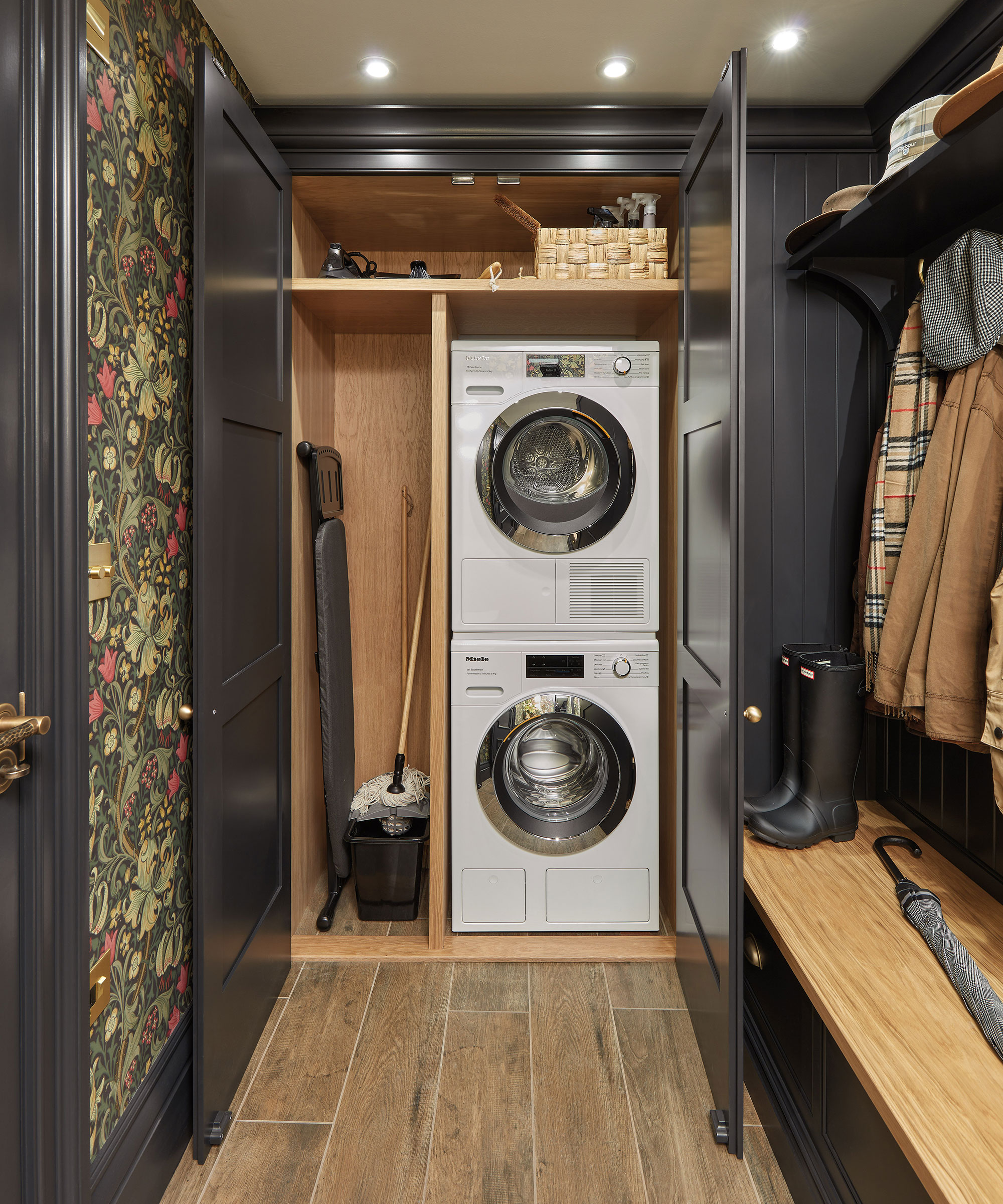 small utility room with wallpaper and stacked washing machine and tumble dryer