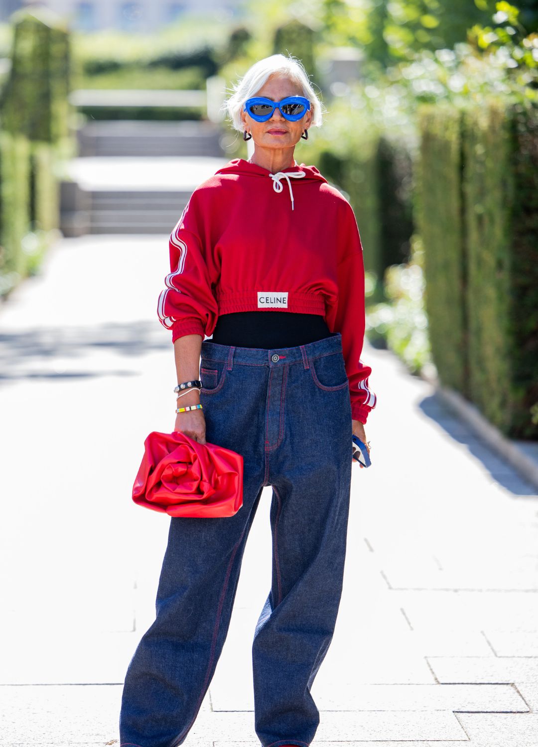 Grece Ghanem wears red cropped Celine hoody, bag, denim jeans, blue Loewe sunglasses outside Lovechild 1979 during day two of the Copenhagen Fashion Week (CPHFW) SS25 on August 06, 2024 in Copenhagen, Denmark.
