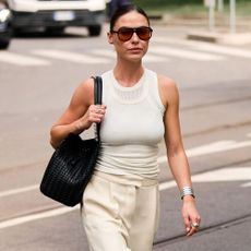 Woman walking down the street with a white tank top, white trousers, and a black shoulder bag