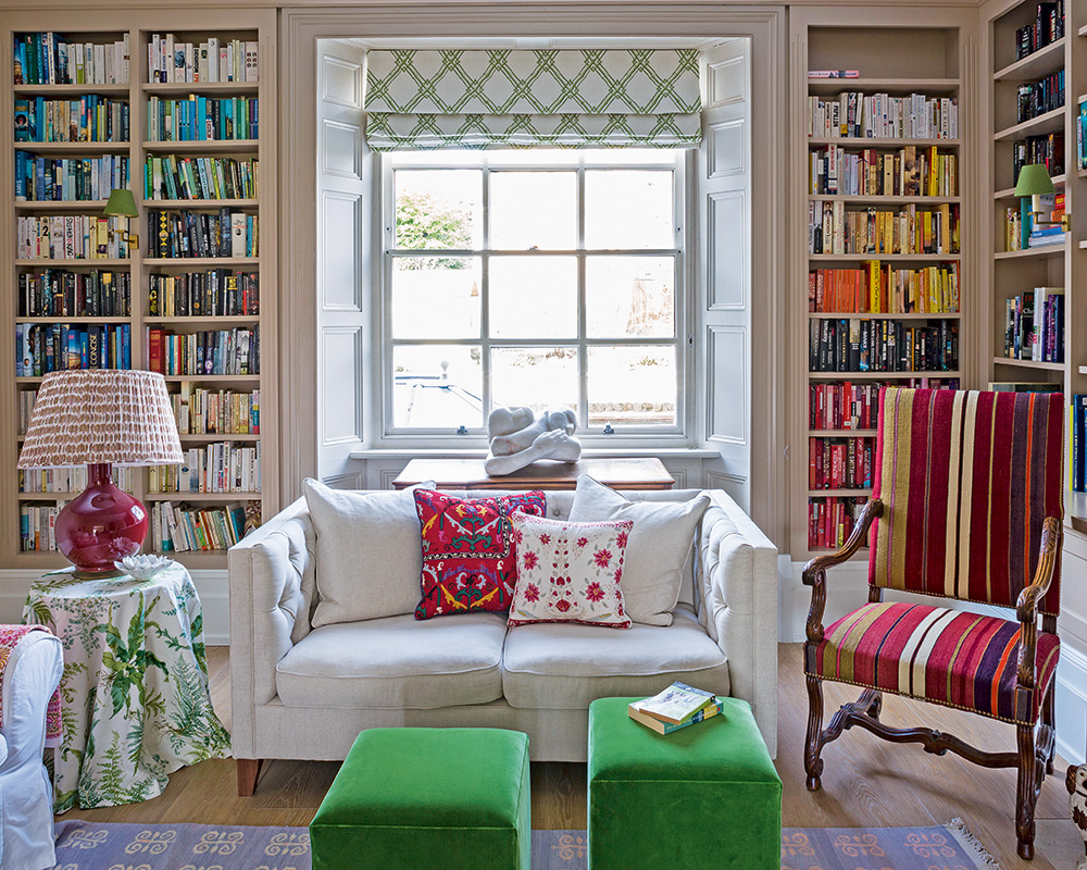 Floor to ceiling color-coded bookcases with a small white sofa and colorful decor.