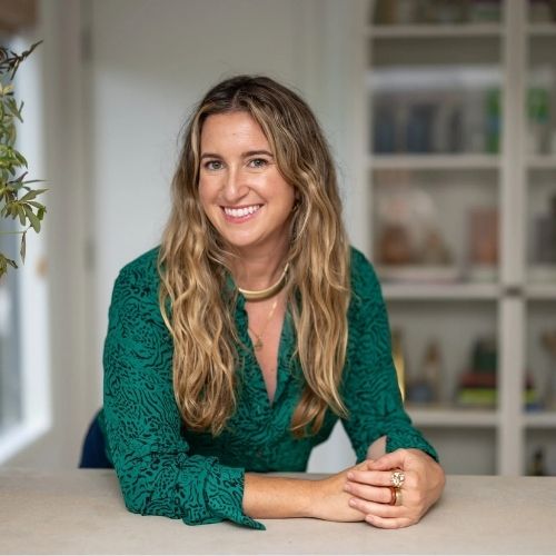 Image of a woman in an emerald green top leaning on a beige counter.