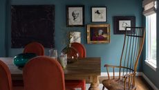 a blue dining room with orange chairs and a gallery wall