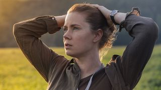 Amy Adams stands with her hands on her head in an open field in Arrival
