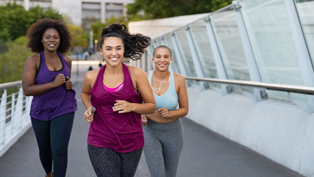 Three smiling women running on bridge in urban environment. They are all wearing leggings and tank tops. 