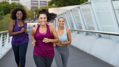 Three smiling women running on bridge in urban environment. They are all wearing leggings and tank tops. 