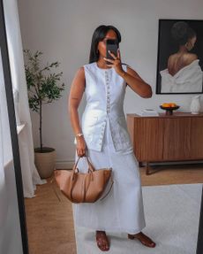 @femmeblk wearing a long vest with a white skirt