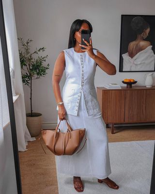 @femmeblk wearing a long vest with a white skirt