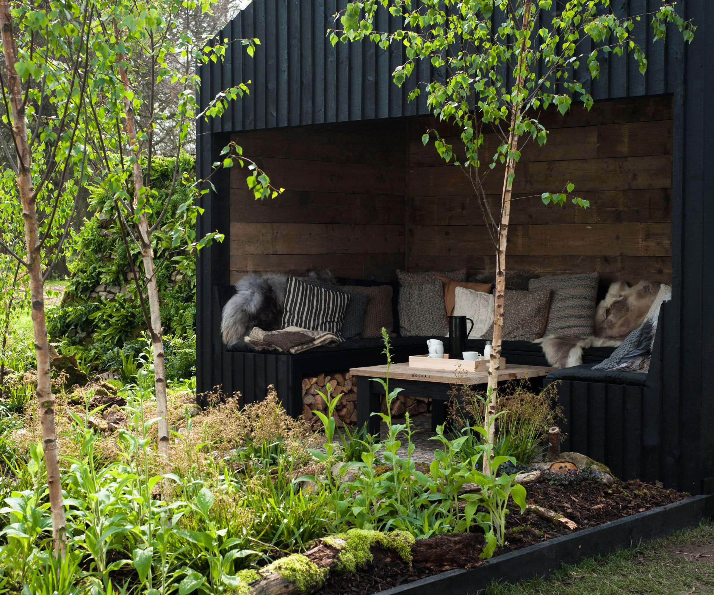 Norwegian garden design with outdoor room, sofa and cushions and flowerbed with plants and young trees