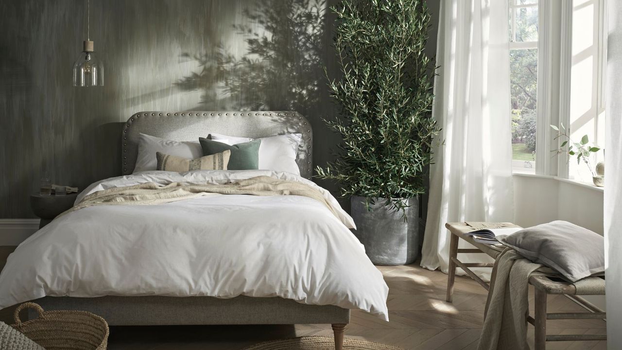 A white bed with a kniet throw blanket in a green bedroom