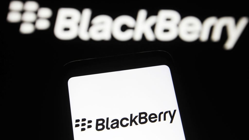 The BlackBerry logo on a smartphone, with the logo on a black wall in the background too