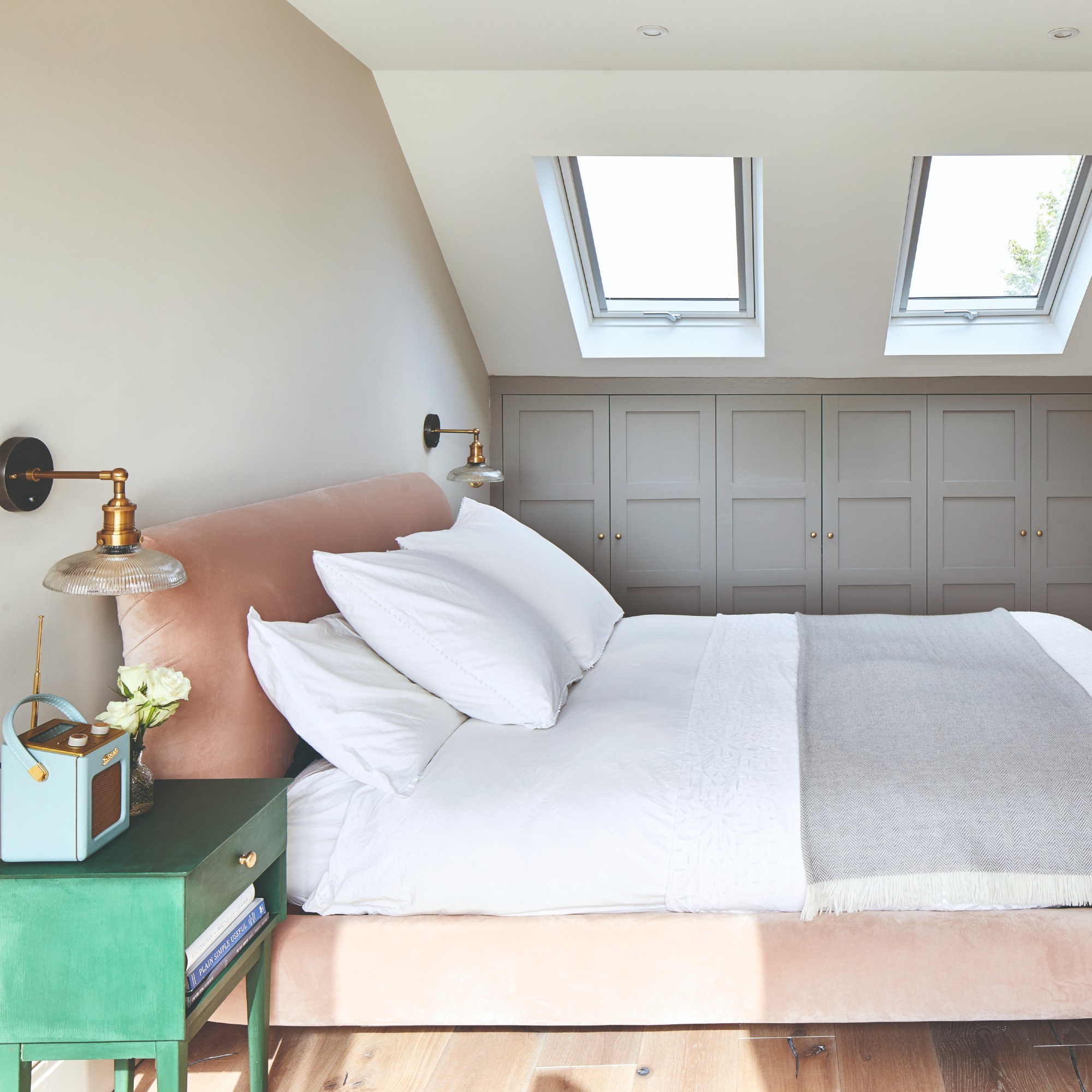 A small bedroom with a pink velvet bed and wall lights above bedside tables