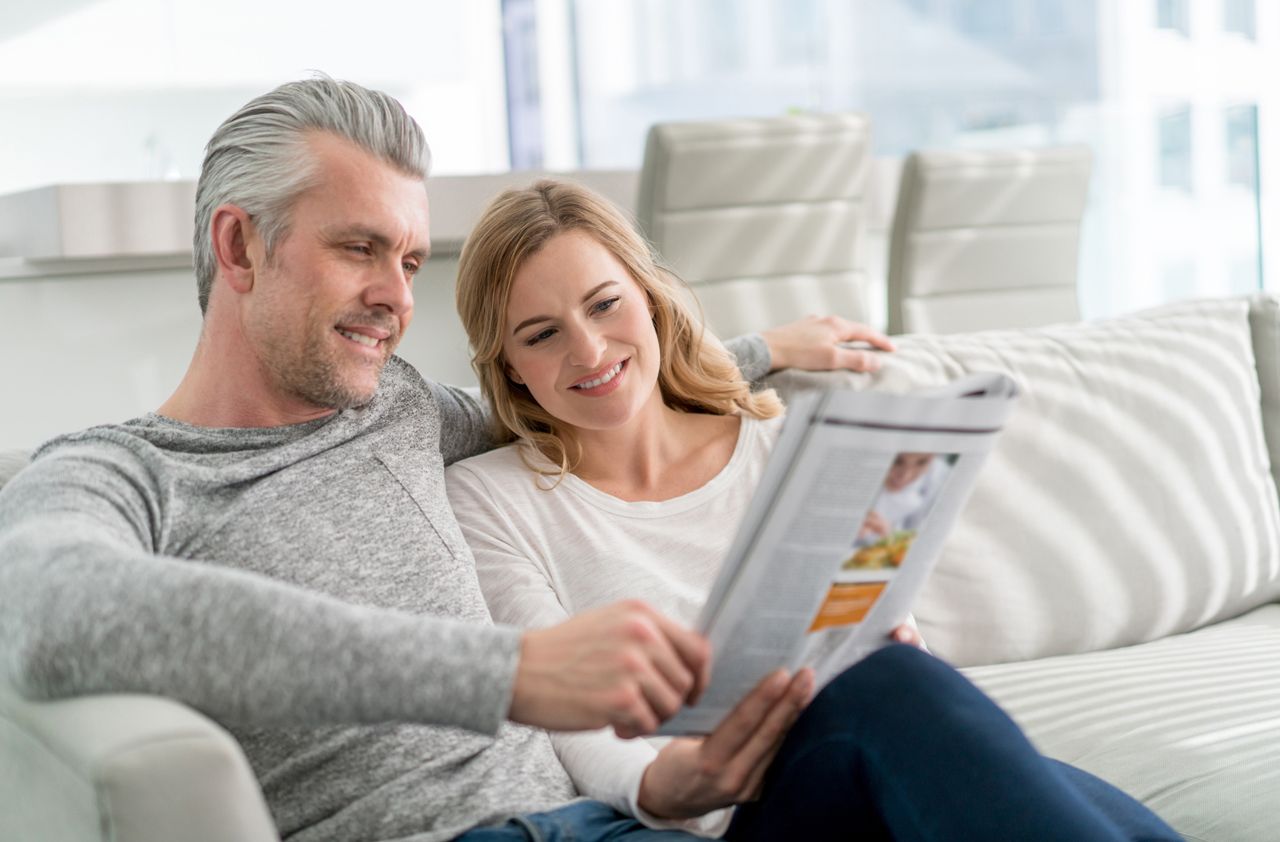 Happy loving couple at home reading a magazine and sitting on the sofa relaxing