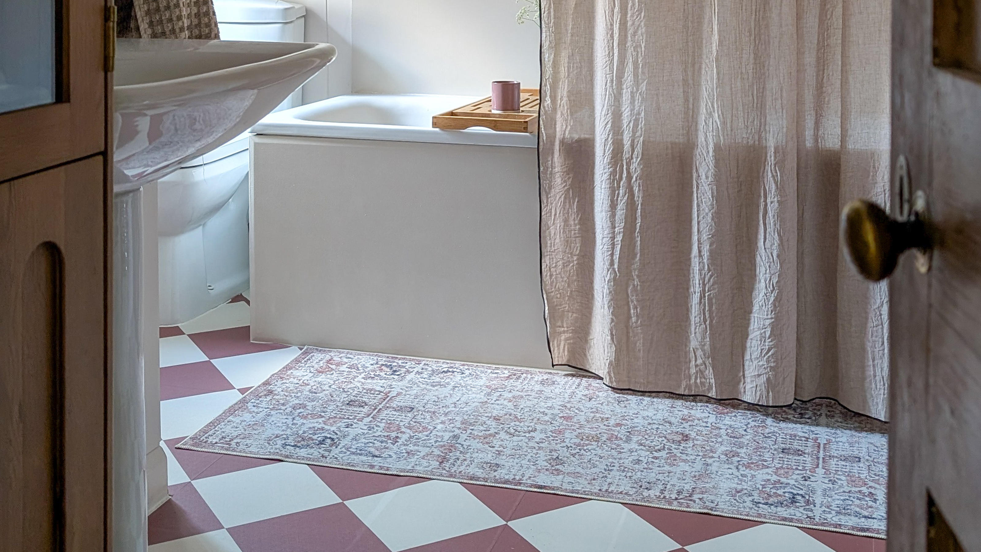 Small neutral bathroom with red and white vinyl checkerboard floor tiles and a soft pink shower curtain