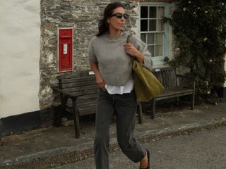 Woman wears a beige sweater over a white tee with faded black straight leg jeans and ballet flats.