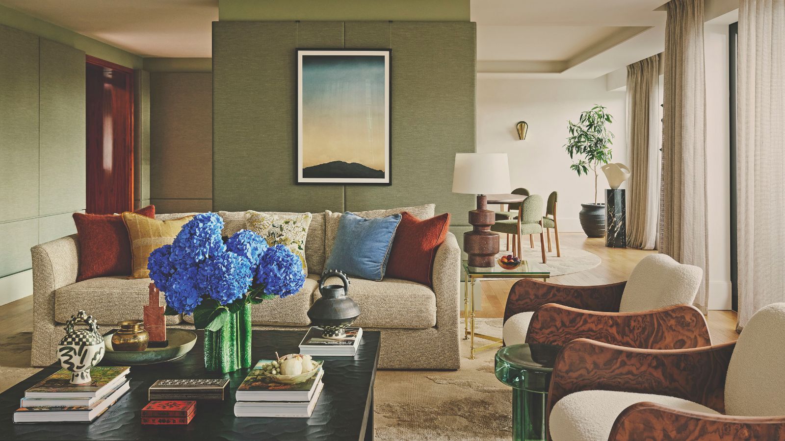 living roo with green walls and sofa and two burl edged armchairs and coffee table stacked with books 