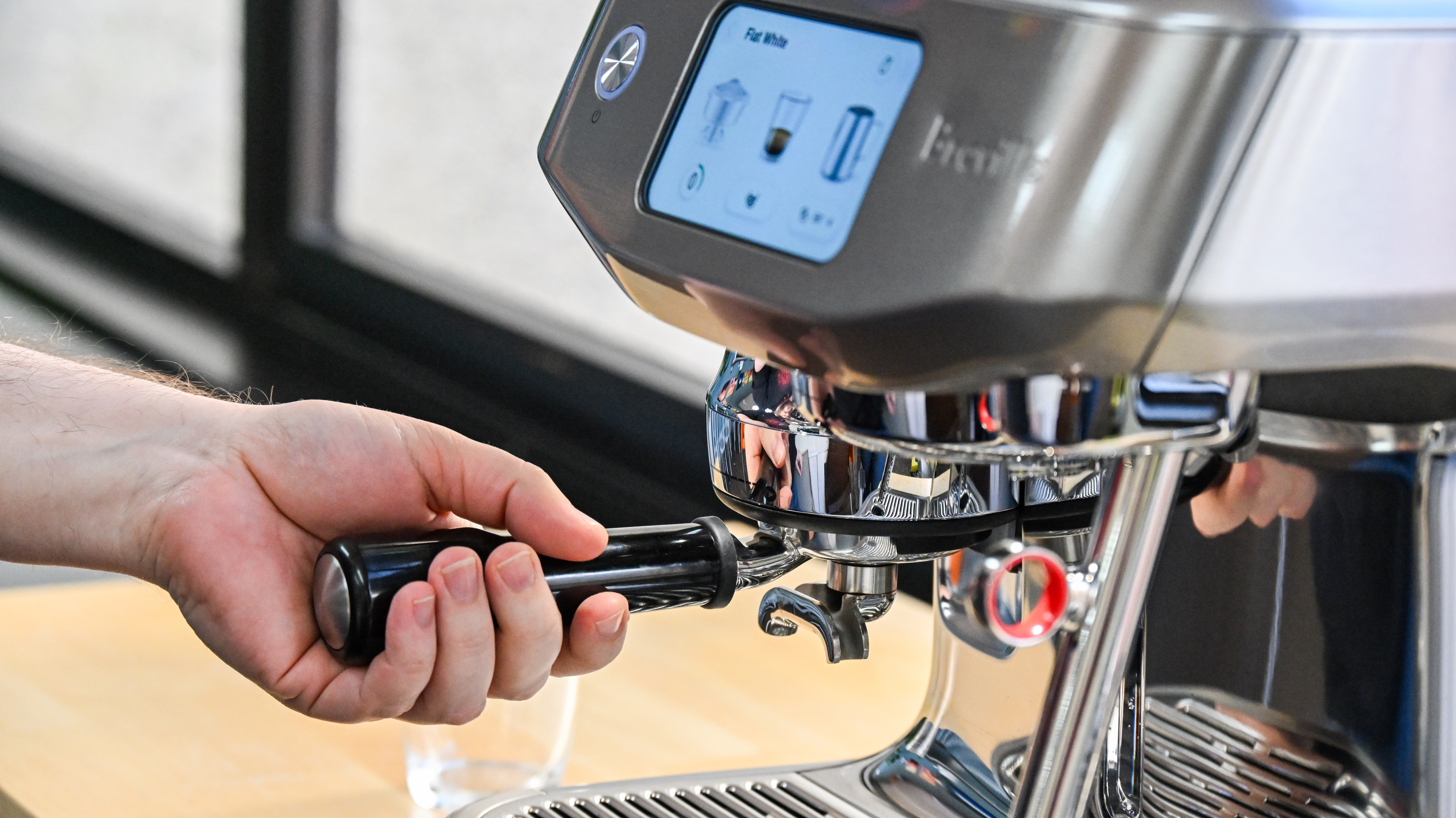 A side-on view of the Breville Oracle Jet coffee machine with a hand inserting the portafilter into the grind outlet.