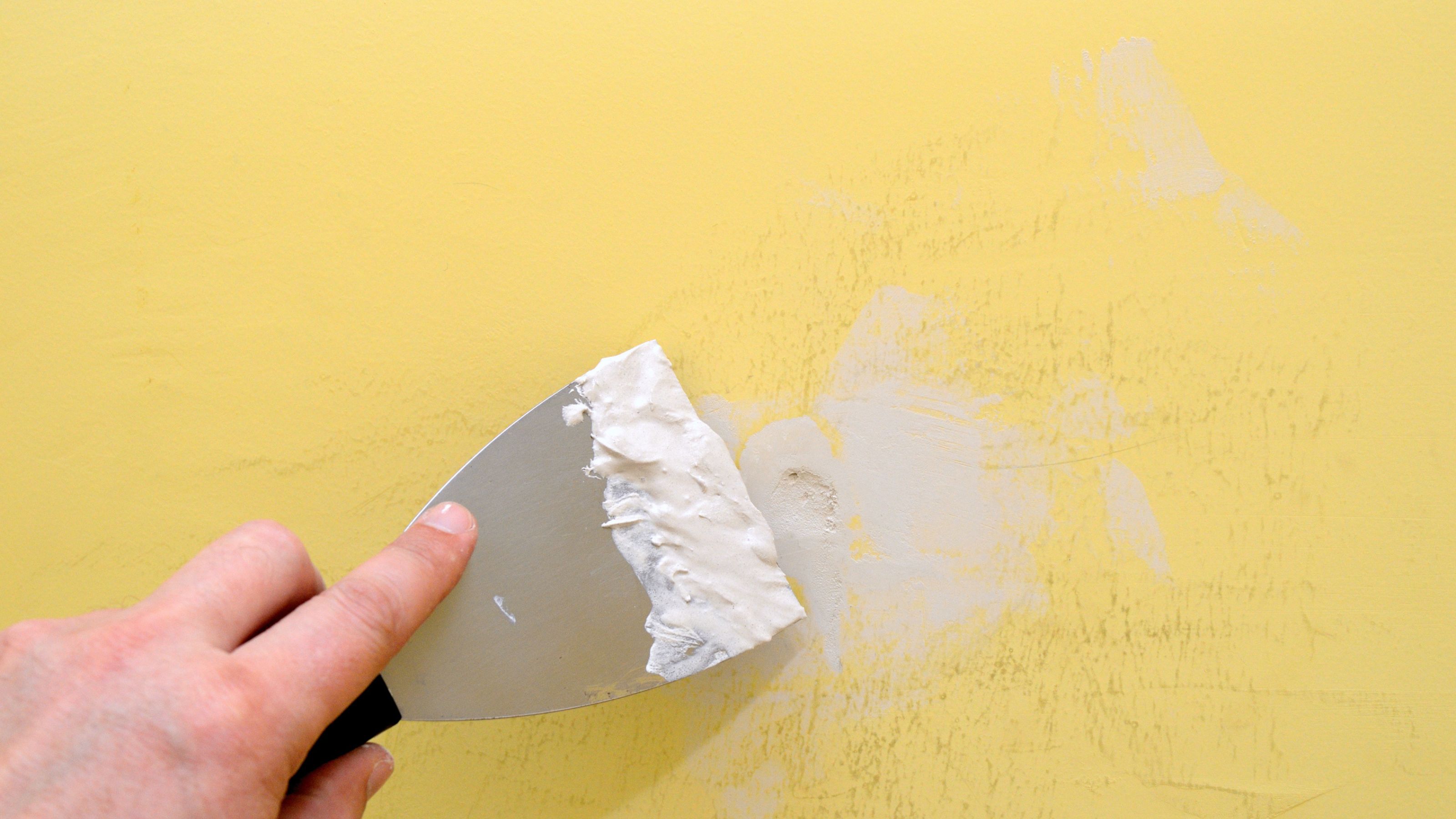 Filling a hole in a yellow wall with filler and a filling knife