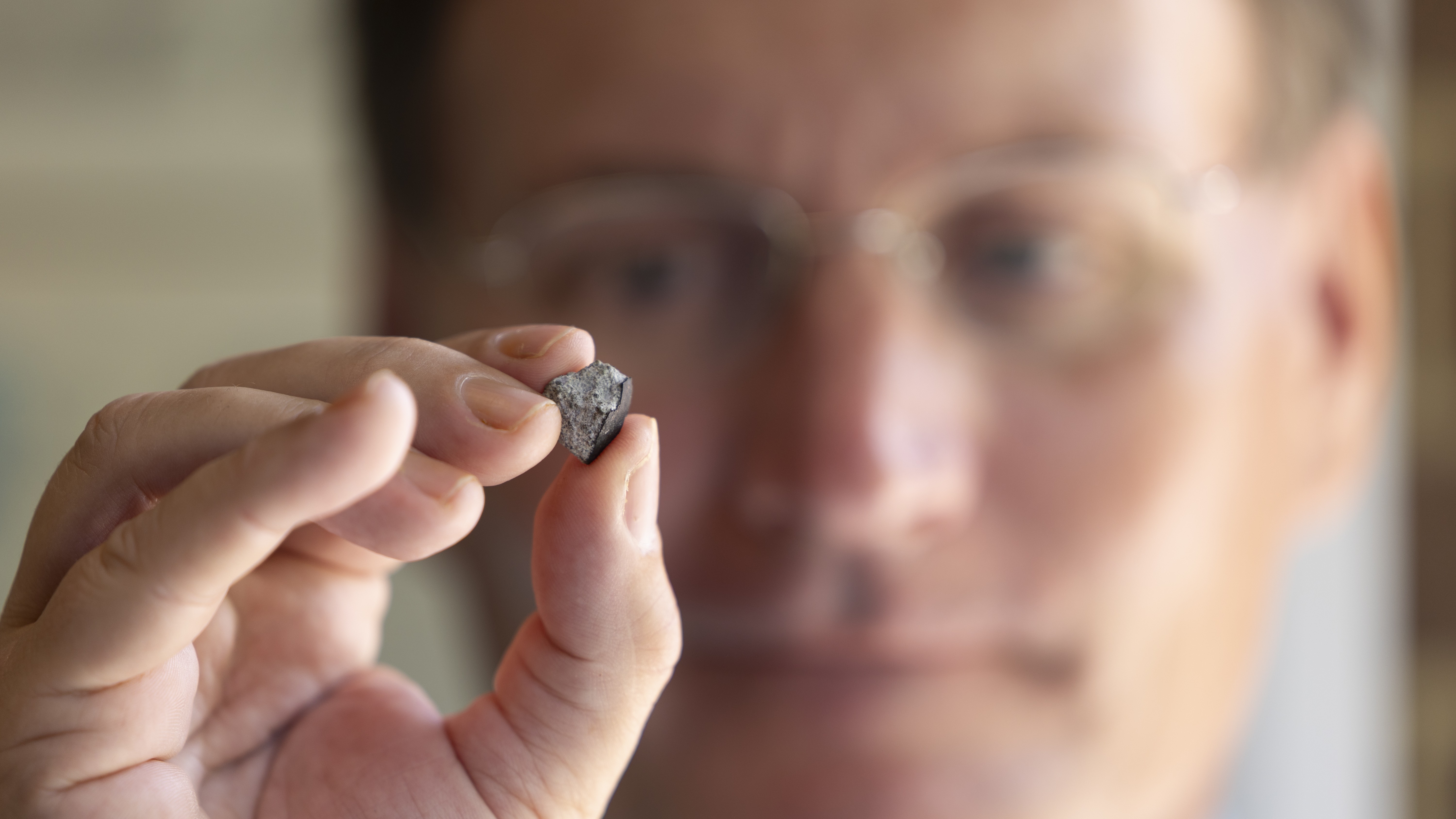A photograph of a researcher holding up a piece of the McDonough Meteorite. 