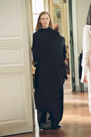 A female model wearing a long black dress walking through a doorway.