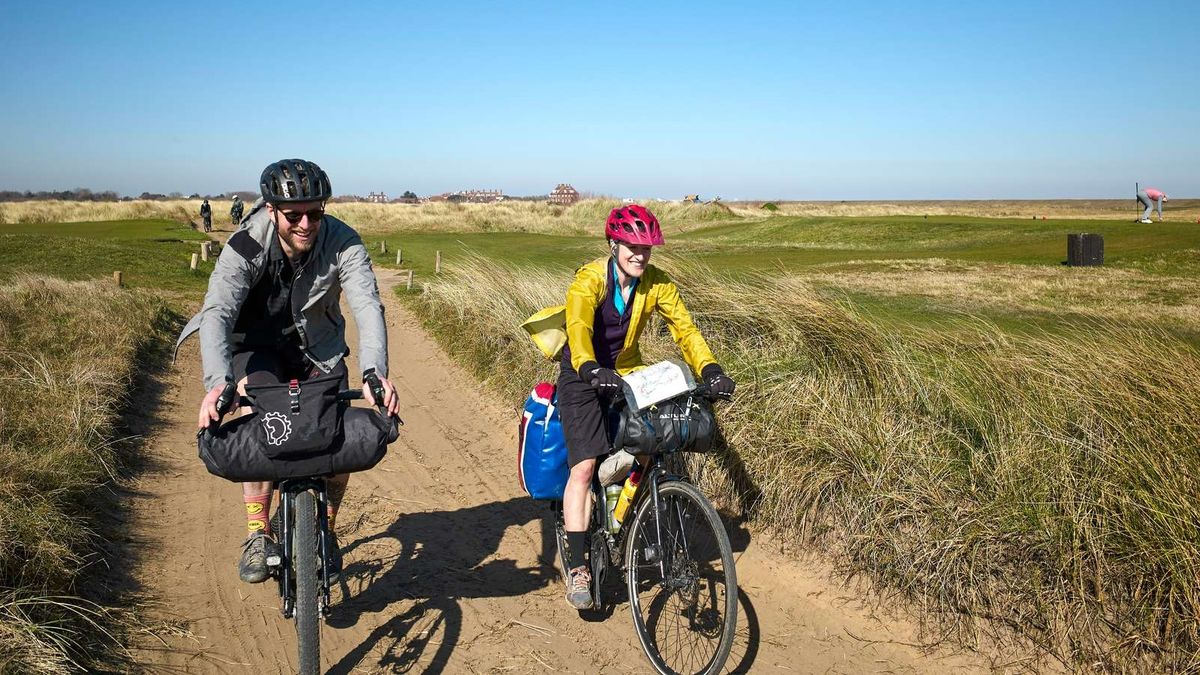 A male and female cyclist riding along a coastal trail in the wind