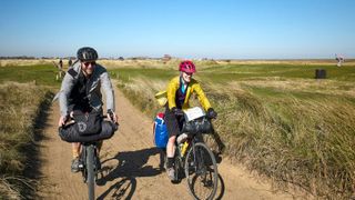 A male and female cyclist riding along a coastal trail in the wind