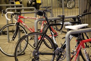 Best bike accessory for security is a bike lock. This image shows three bikes lent up against bike stands, with the middle black bike secured with a lock around the stand and top tube.