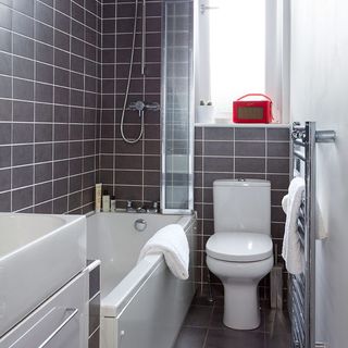 bathroom with grey tiles wall and bathtub with commod