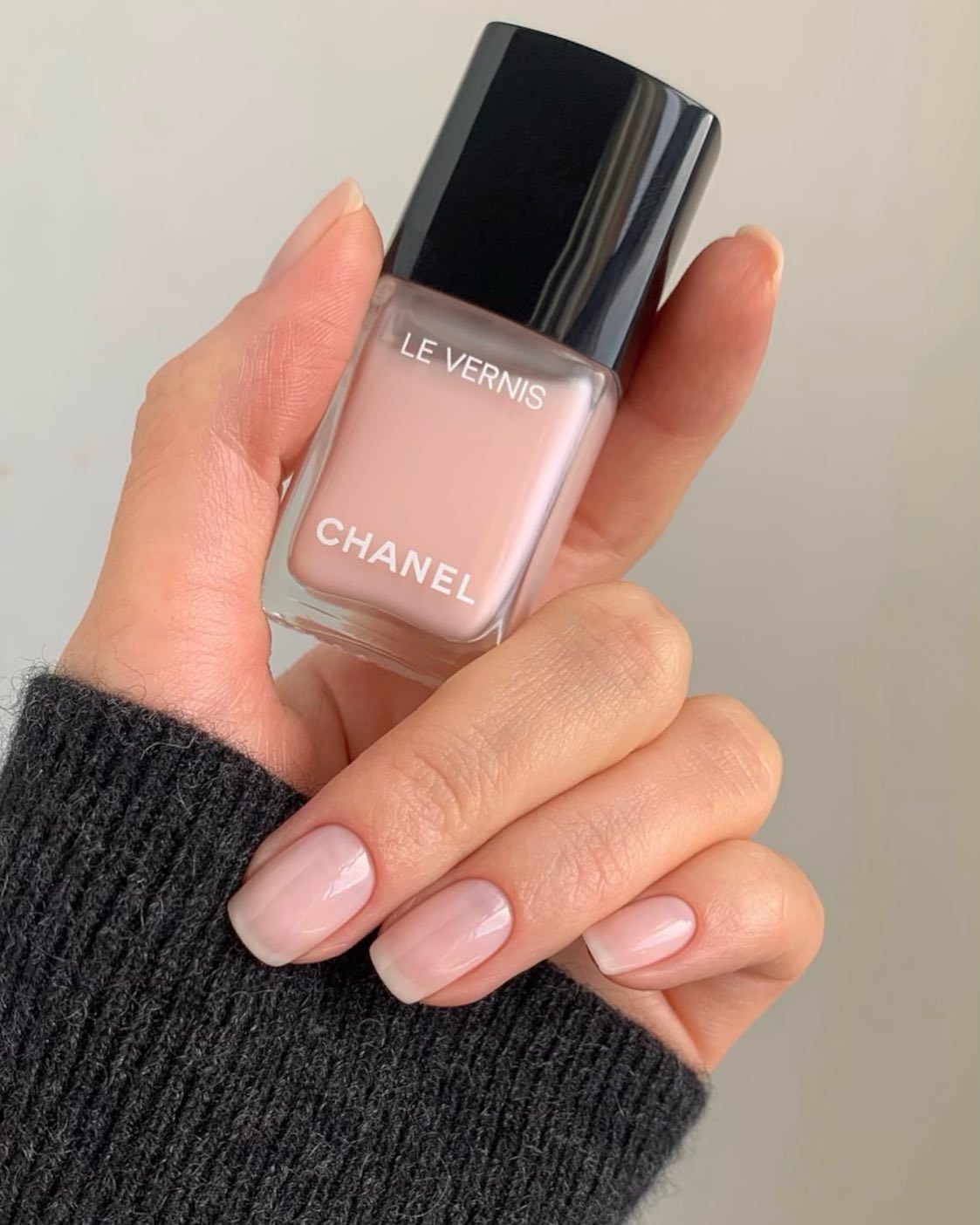 A hand holding a bottle of Chanel ballerina nail polish