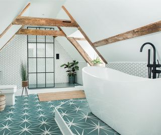 loft conversion bathroom with exposed beams, green tiled floor with white star pattern, freestanding bath and shower at end of room