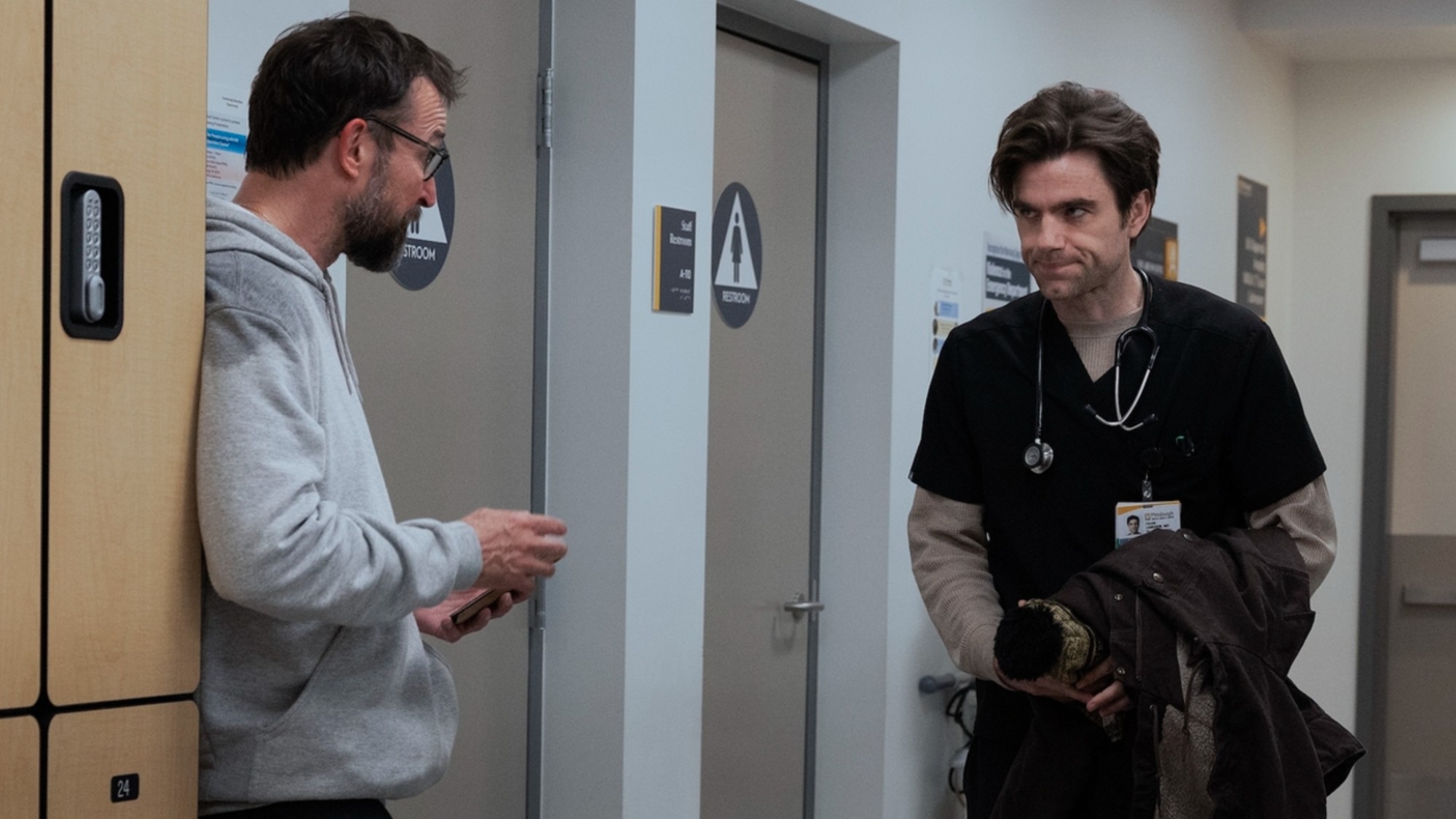 Patrick Ball walking past Noah Wyle in Season 3 of The Pitt.