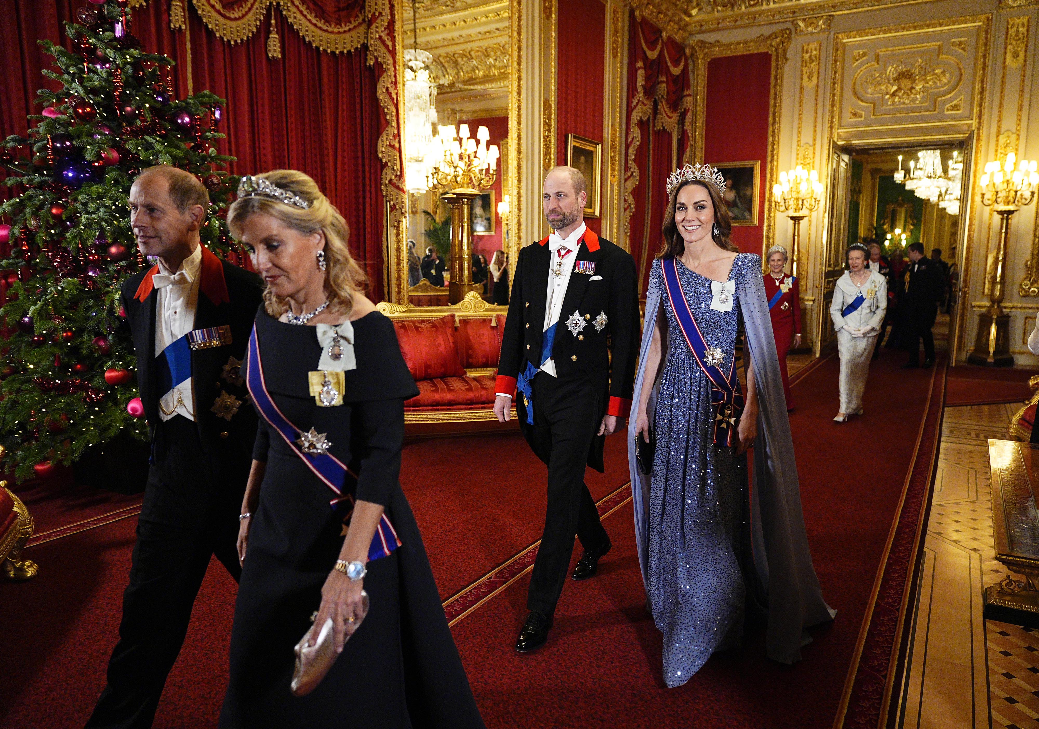 Kate Middleton and Prince William walking past a Christmas tree in evening wear at a state banquet
