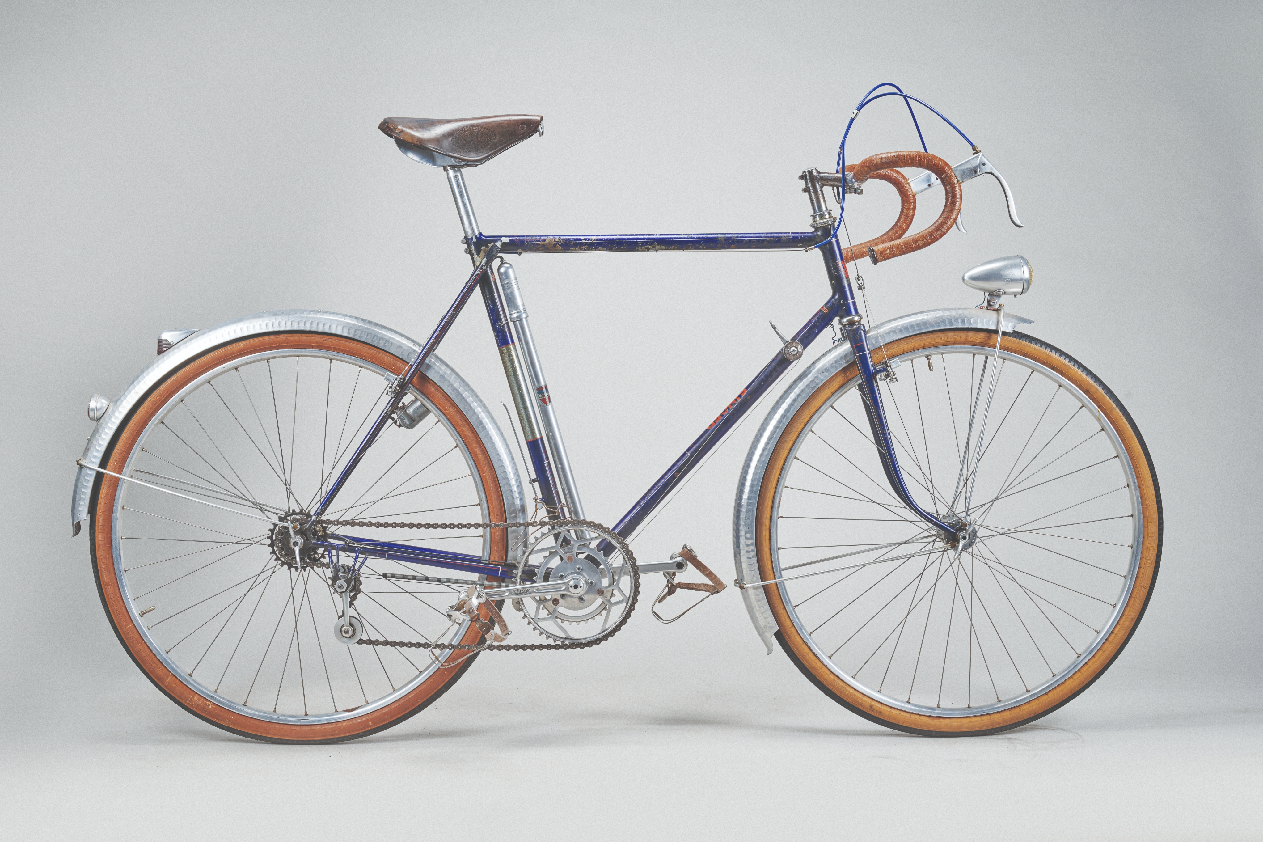 Image of the Alex Singer bike against a plain white background, the frame is blue, saddle is pushed forward in an aggressive position and it features mudguards and lights