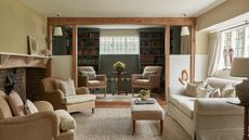 Country cottage living room with cream sofa, beige armchairs, large brick fireplace, green painted library with bookshelves and two armchairs